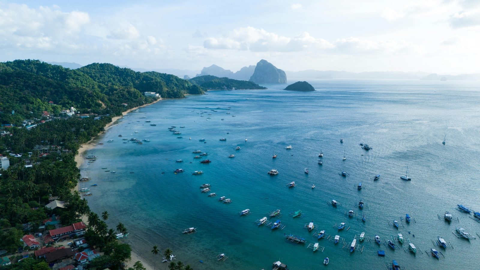 Vue aérienne de la baie d'El Nido : bangkas au mouillage, village en bord de plage et îles calcaires au large